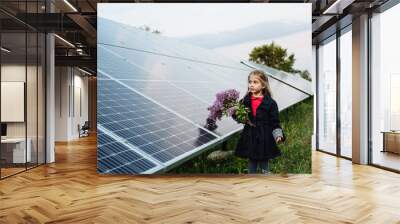 A child with a future of alternative energy and sustainable energy. The child holds flowers on a background of solar panels, photovoltaic. Environmental friendliness and clean energy concept. Wall mural