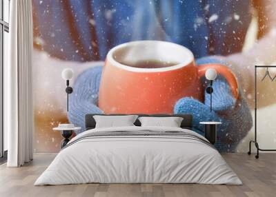 A cup of hot drink, tea or coffee, in winter mittens. Snow falls. New Year concept. Christmas mood. Wall mural