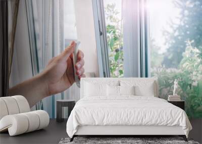 A man's hand holds a plastic window handle.Manual opening white plastic pvc window at home.A man opens a window, closes a plastic frame in his apartment.A man opens a window with a mosquito net. Wall mural