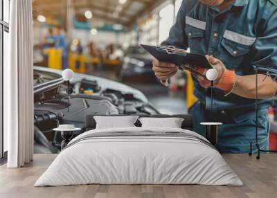 A mechanic in uniform taking notes on a clipboard while working on a car engine at an auto repair shop  Wall mural