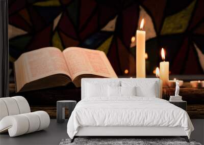 Bible and candle on a old oak wooden table.  Beautiful Stained-glass windows background.Religion concept. Wall mural