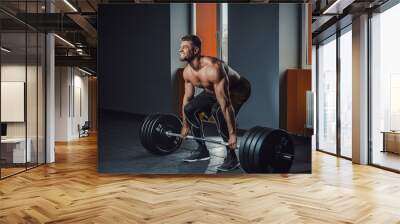 european caucasian athletic man doing deadlift with heavy barbell. man lifting barbell opposite window. emotional moment of lifting weight. affective lifting in gym. posing in gym Wall mural