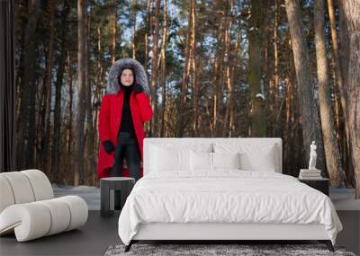 a series of photographs with a young woman in the winter forest. girl in a snowy park. in a red jacket. winter walk in nature. Cold season. Beautiful girl, sunny day. Wall mural