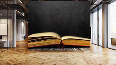 Image of an open antique book on a wooden table with old yellow sheets and dust on a dark background. Side view. Wall mural