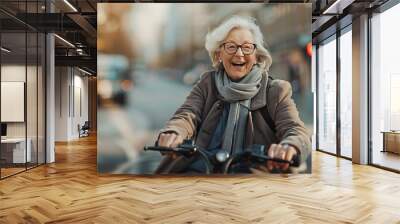 Senior female riding an e-scooter with joy, with blurred city street Wall mural