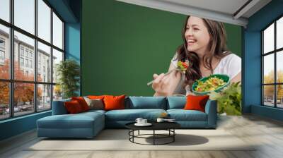 Young woman eating healthy food sitting in the beautiful interior with green wall on the background Wall mural