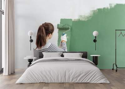 Young woman is painting the wall into green with paint roller in new house Wall mural