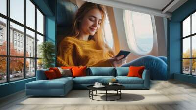 Young woman sitting with phone on the aircraft seat near the window during the flight in the airplane Wall mural