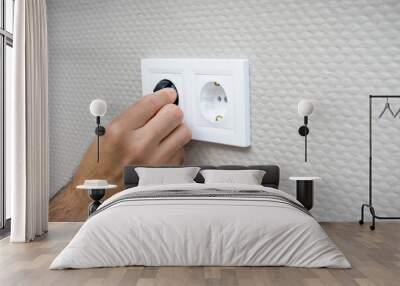 Plugging electrical, black plug in white electric socket on wall. Wall mural