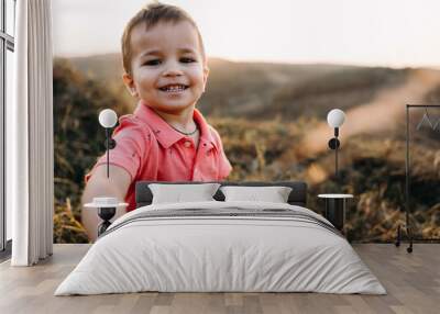 portret of a beautiful young mother in a long red dress with her little son walking on mountain sites on the sunset in summer, dry grass.Mom holds her son's hand and hugs Wall mural