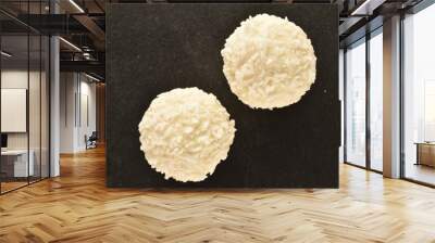 Two round white candies with coconut flakes on a slate board, close-up, top view. Wall mural