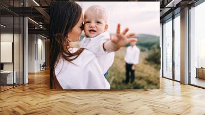 Walk beautiful young family in white clothes with a young son blond in mountainous areas with tall grass at sunset. Mother keeps son in his arms, hugging. family - this is happiness Wall mural