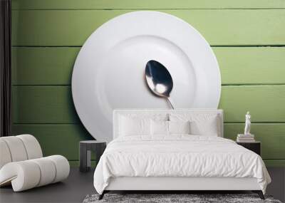 White plate and a fork with a spoon on a green wooden table background. Wall mural