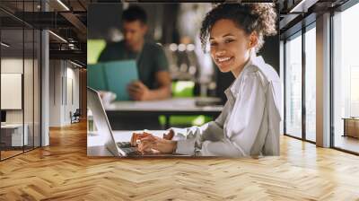 Young curly-haired female office worker sittin at the table in the office Wall mural