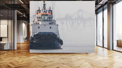  The tug is at the pier in the seaport. The background cranes shrouded in fog. Wall mural