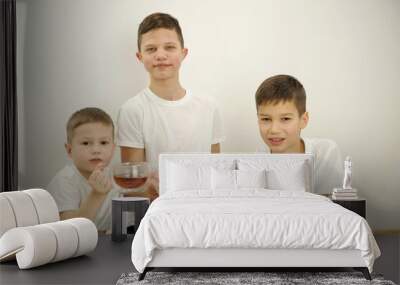 three boys on white background drink tea from glass mugs. They look into frame different ages 5 years old 9 years old 13 years old White t-shirts brothers similar eyes white background teenager Wall mural