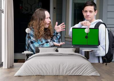 two teenagers in frame boy and girl friend points finger at green chroma key screen on computer laptop girl is surprised with fingers spread open mouth surprised schoolchildren on street ad Wall mural