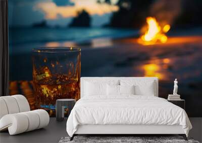 A glass of whiskey or bourbon on a wicker table against the backdrop of a night sandy beach. Burning fire on the shore of a tropical island with sea waves. Wall mural