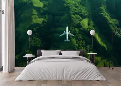 A large passenger airplane flies over green hills and forest. Wall mural