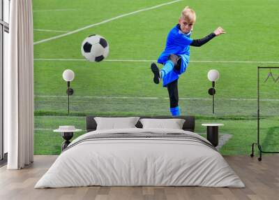 Teenage blonde Caucasian soccer (football) player in blue sport uniform is kicking ball in corner kick during game on grass field on sunny day Wall mural