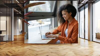 Happy African American woman copywriter working freelance project in modern cafe. Businesswoman using laptop, searching information on website. Successful business. Online training courses concept Wall mural