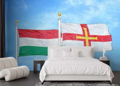 Hungary and Guernsey two flags on flagpoles and blue cloudy sky Wall mural