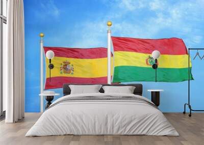 Spain and Bolivia  two flags on flagpoles and blue cloudy sky Wall mural