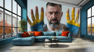 Angry man with drawings of Ukrainian flag against light grey background, focus on palm Wall mural