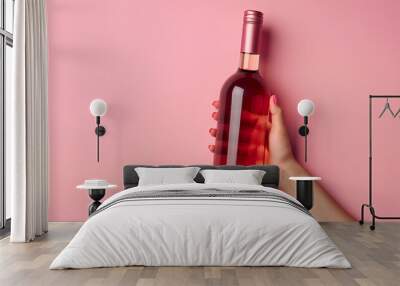 Female hand holding bottle of red wine on pink background Wall mural