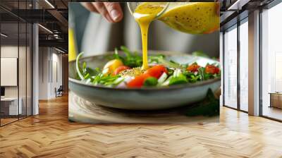 Woman hand pouring honey mustard dressing into bowl with fresh salad on table Wall mural