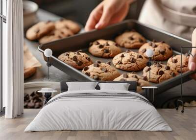 Woman putting baking pan with chocolate chip cookies on table, closeup Wall mural