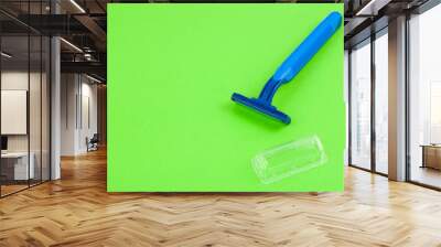 Single new blue plastic disposable razor with two blades and humid strip near transparent cover on blank green paper Wall mural