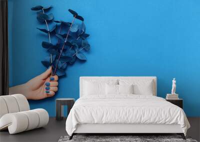 Female hand with trendy blue manicure and branches of eucalyptus on blue background. Wall mural