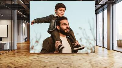 Little boy sitting on father's shoulders. Wall mural