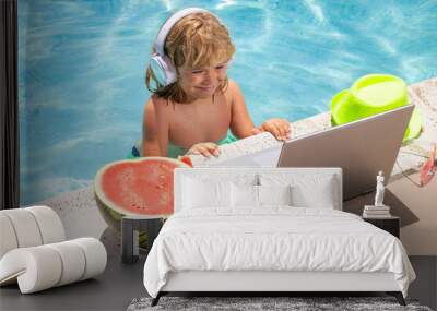 Child relaxing in the pool, using laptop computer in summer water. Kid boy online study or working on tropical sea beach. Technology for life concept. Wall mural