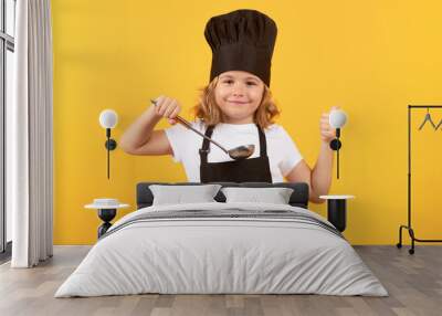 Funny kid chef cook with kitchen ladle, studio portrait. Kid chef cook prepares food on isolated studio background. Kids cooking. Teen boy with apron and chef hat preparing a healthy meal. Wall mural