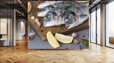 Four sea dorado fish with fragrant spices lie on a wooden board with a large wooden spoon of salt. Cooking process Wall mural