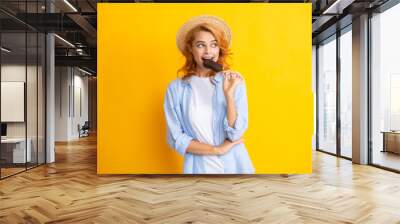 Portrait of redhead girl with chocolate ice cream on yellow background. Curly cheerful woman eating ice cream. Wall mural