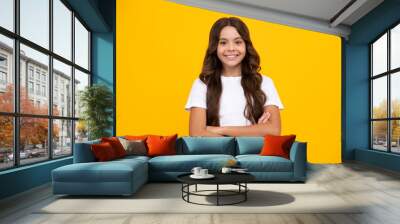 Portrait of young teenage girl standing with crossed arms against yellow background with copy space. Wall mural