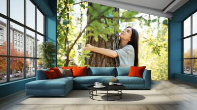 Young woman embracing a tree while enjoying nature in a sunlit forest during summer Wall mural