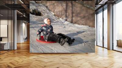 Little girl moving fast from snowy hill on snow sled in winter Wall mural