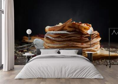 two stacks of pancakes, two folded pancakes, sprinkled with berries, cookies, sugar powder and caramel syrup on parchment on a dark wooden table Wall mural