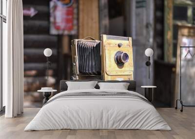 Vintage camera on a tripod on the background of an old wooden hut. A camera from the late 19th or early 20th century.  Wall mural