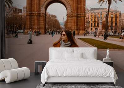 BARCELONA, SPAIN, January 17,2019.  Girl on the background the arch of Triumph in Barcelona. Cute young girl posing in autumn park. She is wearing mustard coat and glasses.  Wall mural