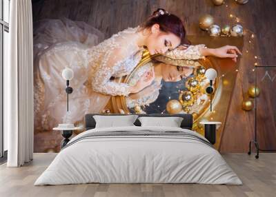 beautiful young girl in gold glamorous near christmas balls and toys looks in the mirror Wall mural