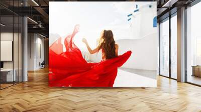 Fashion outdoor photo of gorgeous young woman with red hair in airy red dress posing on the streets of Oia, Santorini, Greece.  Wall mural