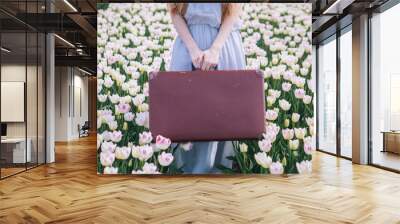 Beautiful young woman with long red hair wearing in white dress standing with luggage on colorful tulip field. Happy blond girl holding old vintage suitcase. Spring travel and adventure concept Wall mural