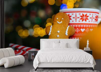 Christmas postcard with gingerbread man red mug with christmas ornament on light bokeh from Xmas tree and red striped holidays candies. Xmas candies and cup with marshmallow on wood background. Wall mural