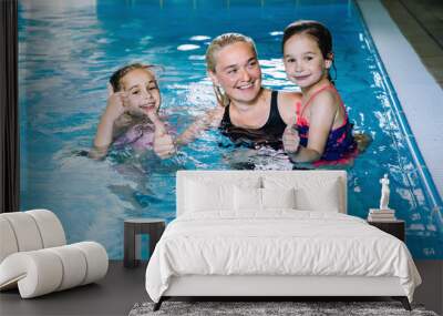 Mother with two daughters having fun in indoor swimming-pool. Girl is resting at the water park. Swimming school for small children. Concept friendly family sport summer vacation. Selective focus. Wall mural