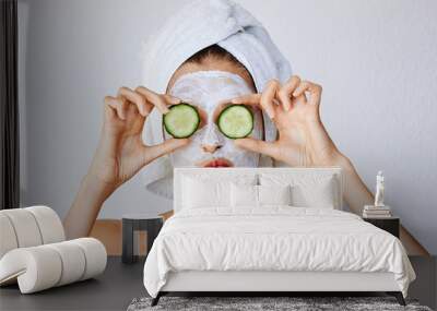 beautiful young woman with facial mask on her face holding slices of cucumber. skin care and treatme Wall mural